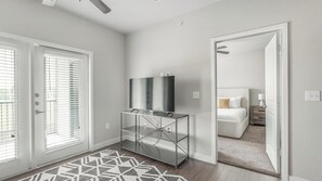 A modern hotel room with a glass console table, a flat-screen TV, and a bed with a nightstand. - Landing | Stunning 1BD, Clubhouse, Courtyard (Katy)