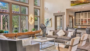 A spacious living room with large windows, a modern sofa, a coffee table, and a kitchen area visible through an open door. - Landing | Stylish 1BD, Game Room, Pool (Haltom City)