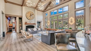 A spacious living room with a fireplace, large windows, and a modern chandelier. - Landing | Stylish 1BD, Game Room, Pool (Haltom City)