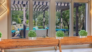 A view through large windows of a patio area with outdoor seating and a pergola. - Landing | Stylish 1BD, Game Room, Pool (Haltom City)