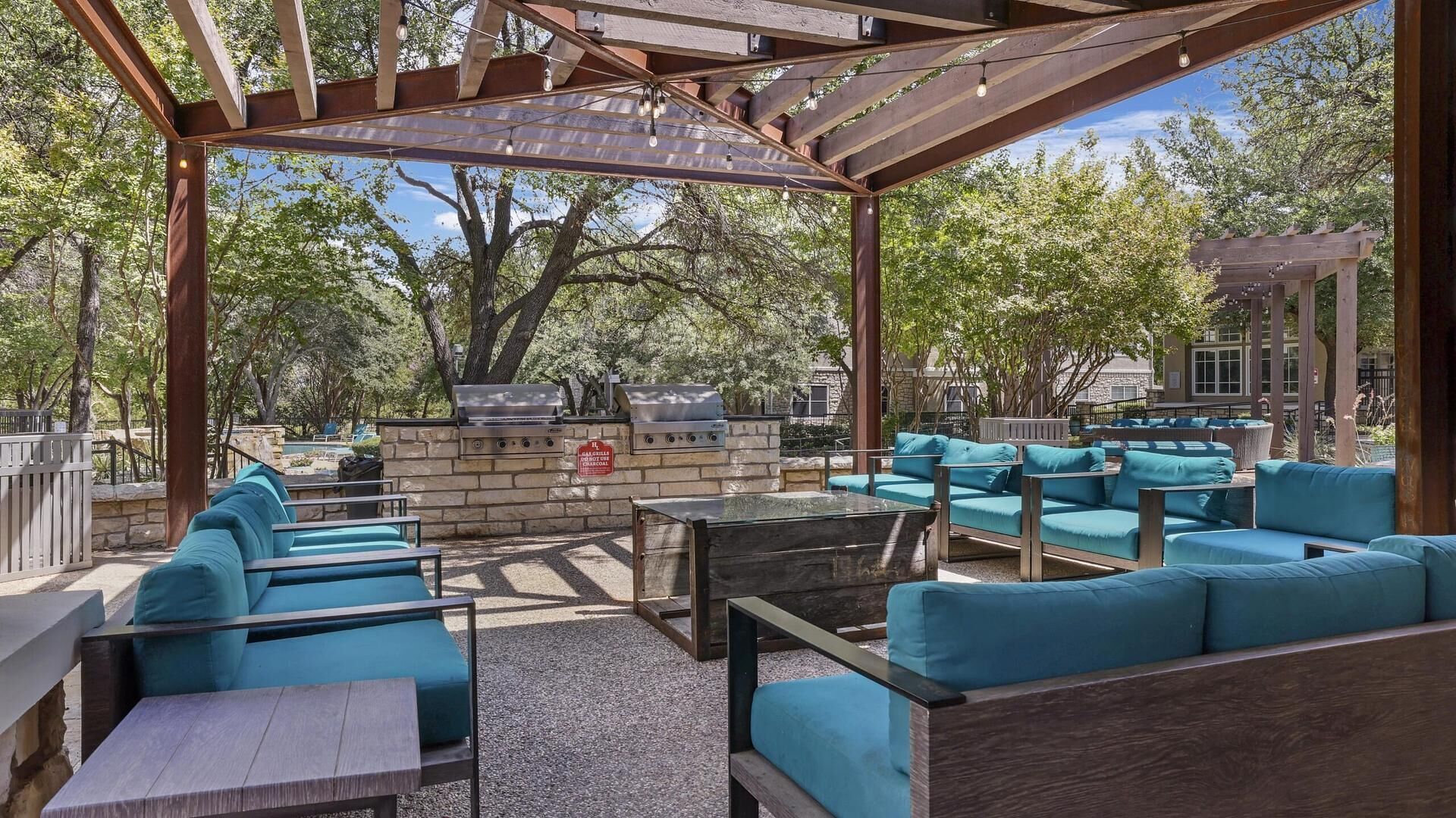 An outdoor patio with blue cushioned seating, a stone barbecue station, and a pergola structure.