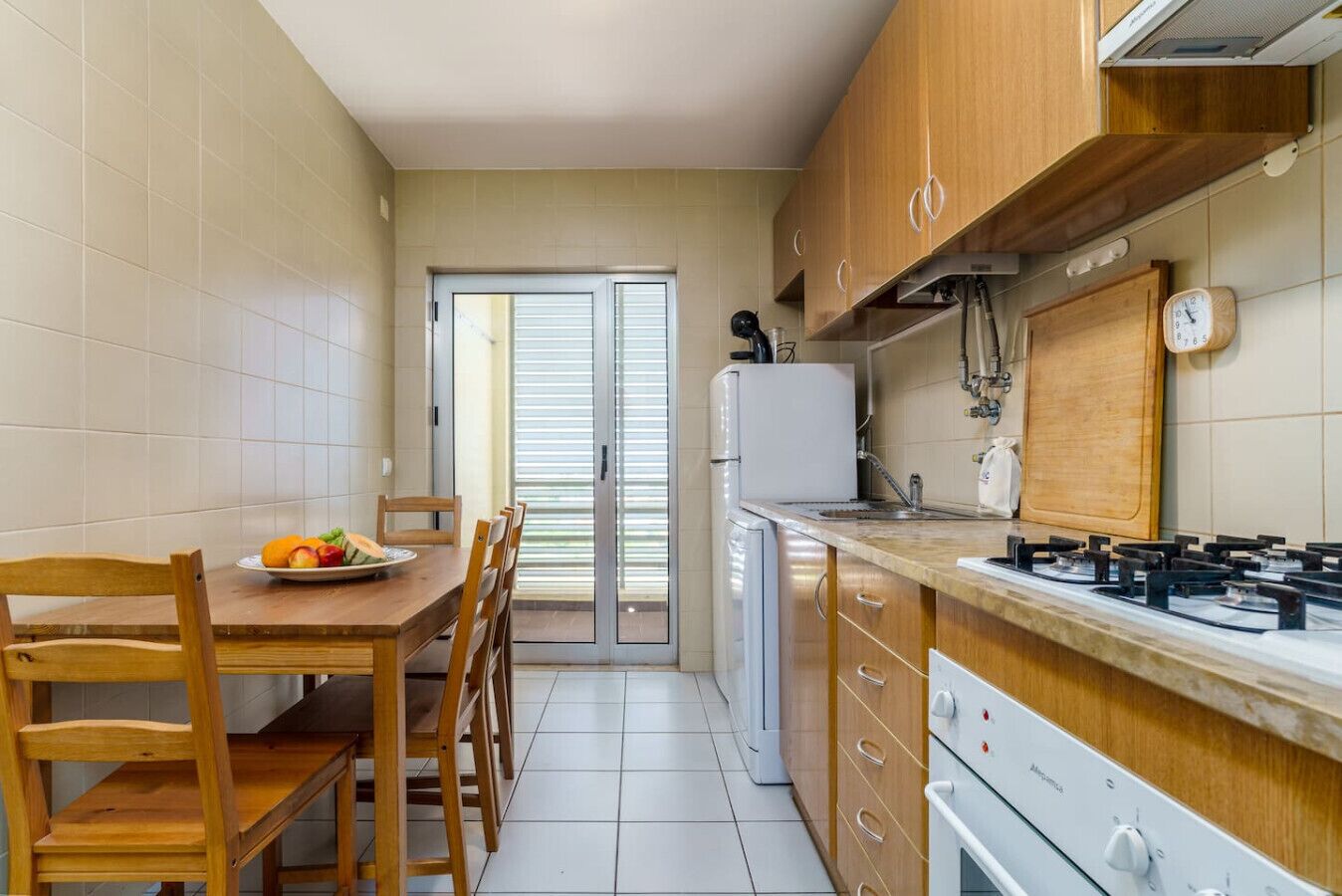 A compact kitchen with wooden cabinets, a gas stove, a refrigerator, and a dining area with a table and chairs.