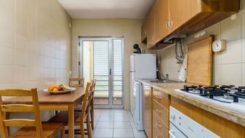 A compact kitchen with wooden cabinets, a gas stove, a refrigerator, and a dining area with a table and chairs.