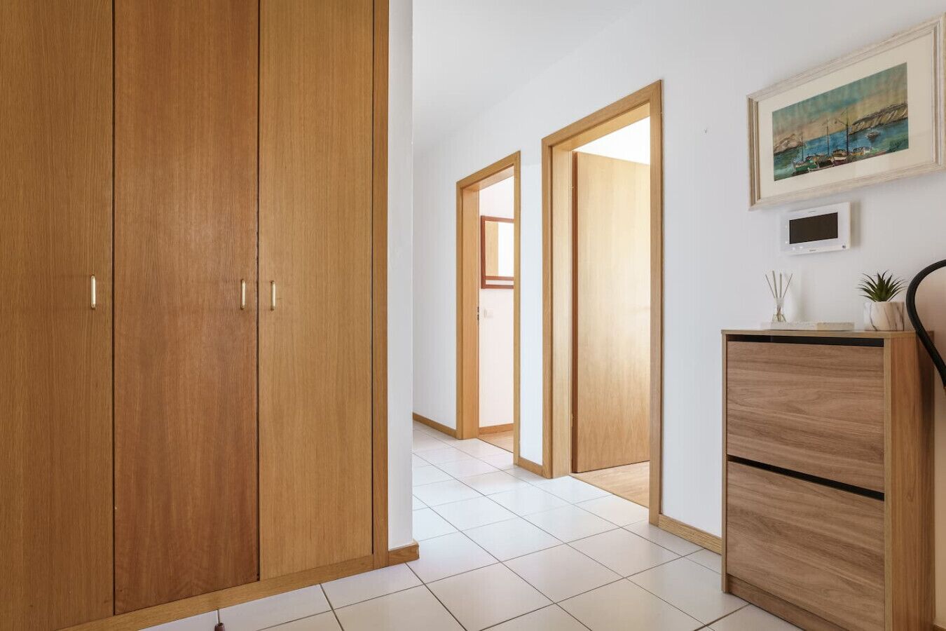 A hallway with wooden wardrobes, a tiled floor, and a painting on the wall.