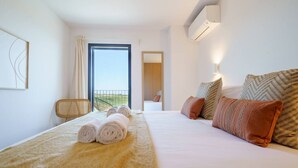 A hotel room with a bed, a window with a view, a door, and an air conditioning unit.