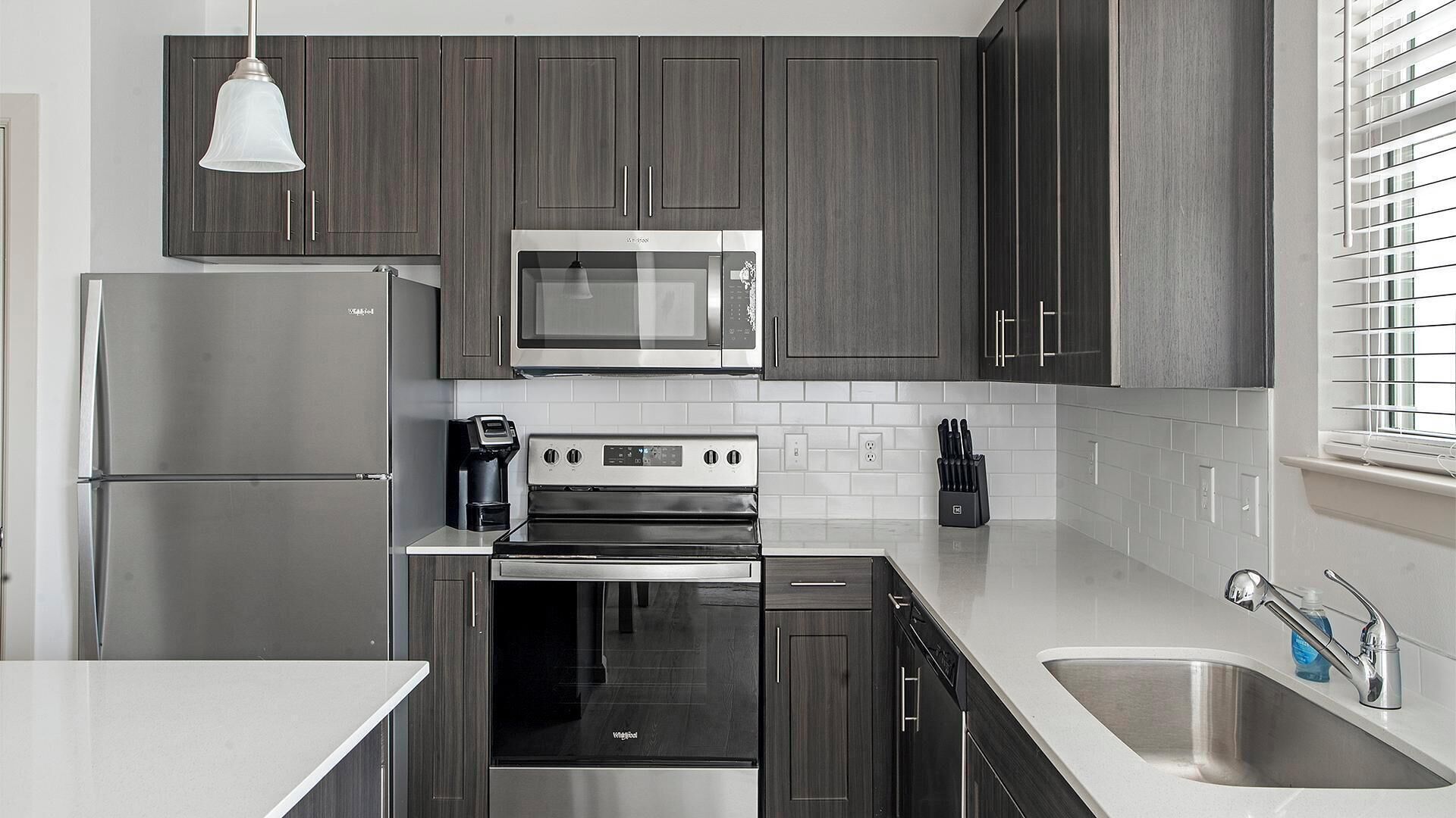 Une cuisine moderne avec des meubles en bois foncé, des appareils électroménagers en acier inoxydable et un plan de travail blanc.