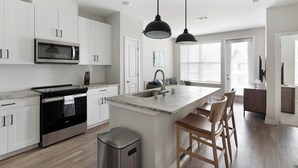 Une cuisine moderne avec des meubles blancs, une cuisinière en acier inoxydable, un four à micro-ondes et un grand îlot central doté de tabourets de bar.