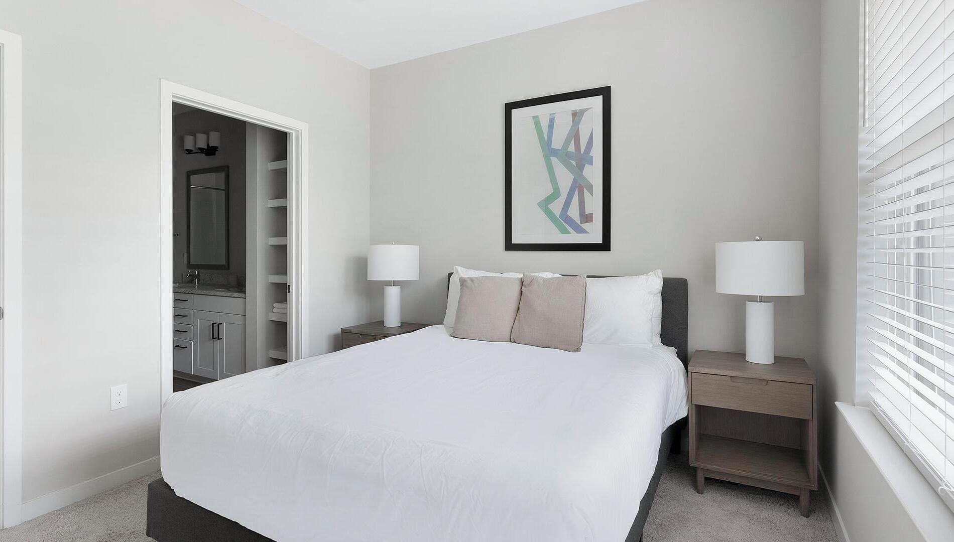 A bedroom with a bed, two bedside tables with lamps, a closet, and a window with blinds.