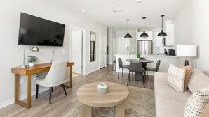 Ein modernes Wohnzimmer mit Fernseher, Essbereich und Küche.