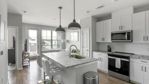 A modern kitchen with white cabinets, a central island with bar stools, a built-in microwave, and an oven.