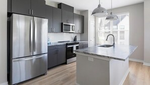A modern kitchen with stainless steel appliances, a central island with a sink, and pendant lighting. - Landing | Beautiful 2BD, Pool, Clubhouse (Huntsville)