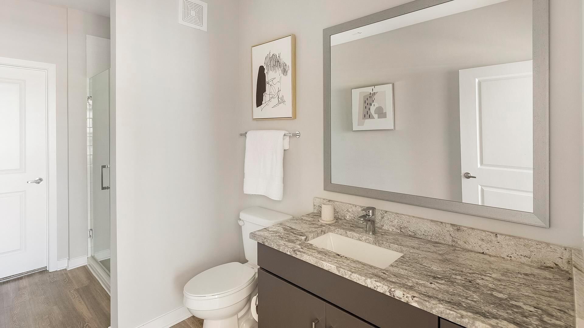Une salle de bain moderne avec un comptoir en marbre, un grand miroir et deux œuvres d’art encadrées.