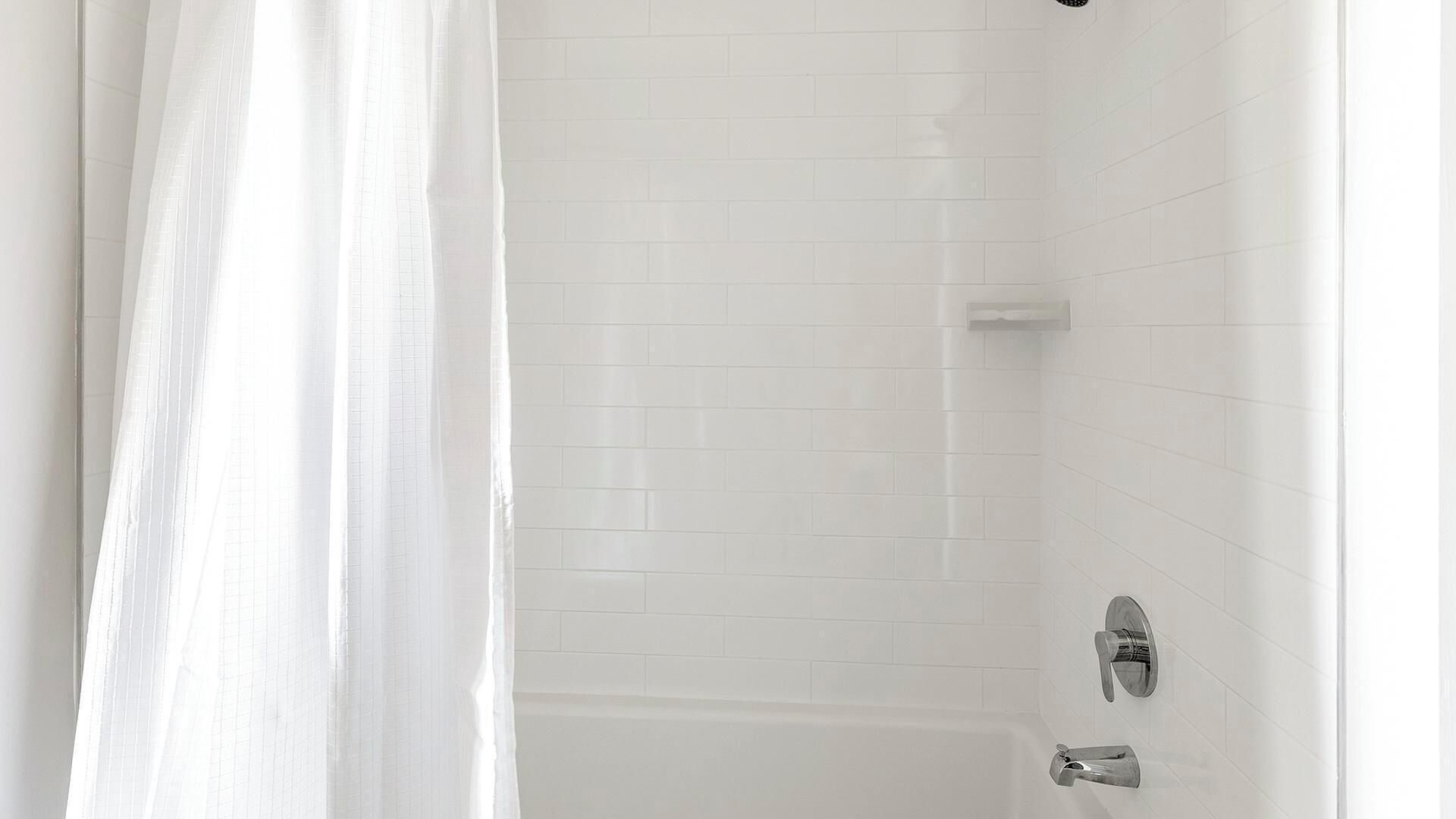 A bathroom with white tiled walls, a shower curtain, and a bathtub with a faucet.
