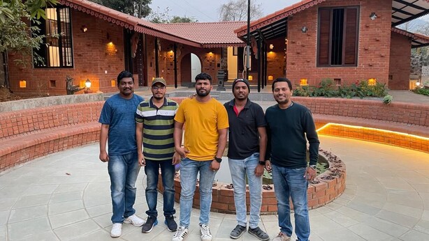 Un grupo de cinco hombres de pie frente a un edificio de ladrillo con techo de tejas y un patio circular.
