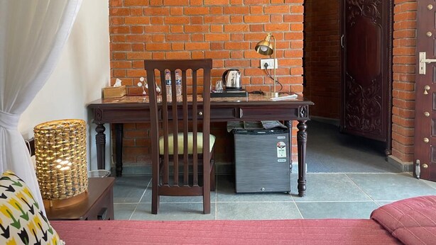 Una habitación con pared de ladrillo, un escritorio de madera, una silla, una lámpara, un armario y una puerta.