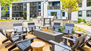 Een terras met buitenmeubilair in moderne stijl, een tafel met glazen blad en een barbecue.