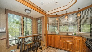 A kitchen with wooden cabinets, a dining area with stools, and large windows with blinds. - Charming rental in Rocky Top, TN-walking distance to Norris lake and marina! (Rocky Top)