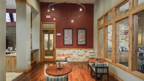 A cozy interior with wooden floors, two round tables with chairs, a stone accent wall, and a large window with a view.