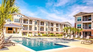 A multi-story residential building with a swimming pool and lounge chairs. - Landing | Incredible 1BD, Pool, Clubhouse (Austin)