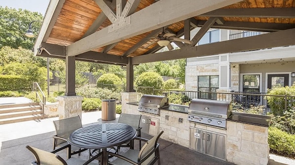 An outdoor patio with a stone grill station, a round table, and chairs.
