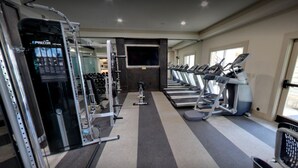 Une salle de sport équipée de tapis de course, d’appareils de musculation et d’un écran de télévision.