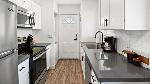 A modern kitchen with white cabinets, stainless steel appliances, and a wooden floor. - Sunrise Vista-walk to Downtown Old Town & Bars! (Scottsdale)
