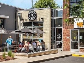 Un espace extérieur aménagé avec des parasols, un bâtiment en briques et une devanture de magasin avec une enseigne.