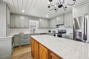 A modern kitchen with light grey cabinets, a large island, stainless steel appliances, and a wooden floor.