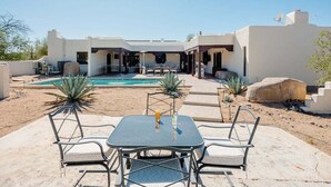 A poolside area with a table and chairs, a pool, and a building with a patio. - Bed Rock Desert -pool Heat Available - Spring Break (Cave Creek)