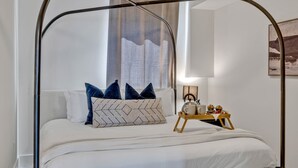 A neatly made bed with a metal canopy, a bedside table with a lamp, and a window with curtains. - Euphony-designer Furnishings-5 Mins to Broadway (Nashville)