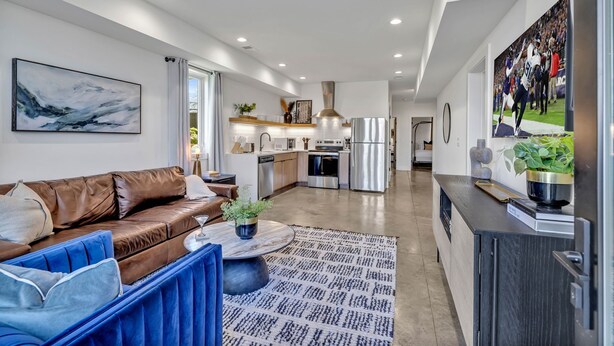 A modern kitchen with stainless steel appliances, a dining area with a brown leather sofa and blue chairs, and a living room with a large abstract painting. - Euphony-designer Furnishings-5 Mins to Broadway (Nashville)