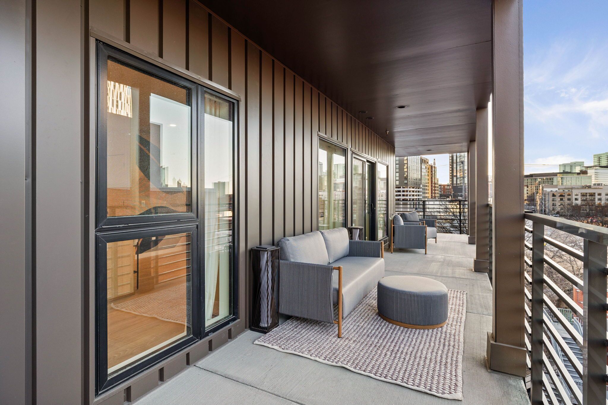 A modern balcony with a sofa, ottoman, and a patterned rug.