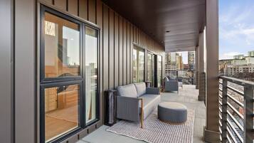 A modern balcony with a sofa, ottoman, and a patterned rug.