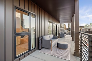 En moderne balkon med sofa, skammel og et mønstret tæppe.