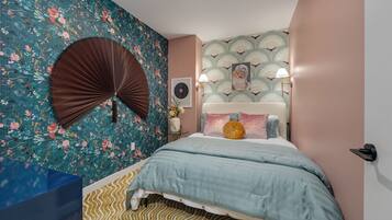 A bedroom with a bed, a wall fan, and a patterned wallpaper.