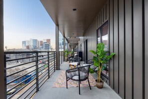 Un balcón con vistas a la ciudad, que incluye una zona de estar con sillas y una mesa, una planta en maceta y una alfombra estampada.