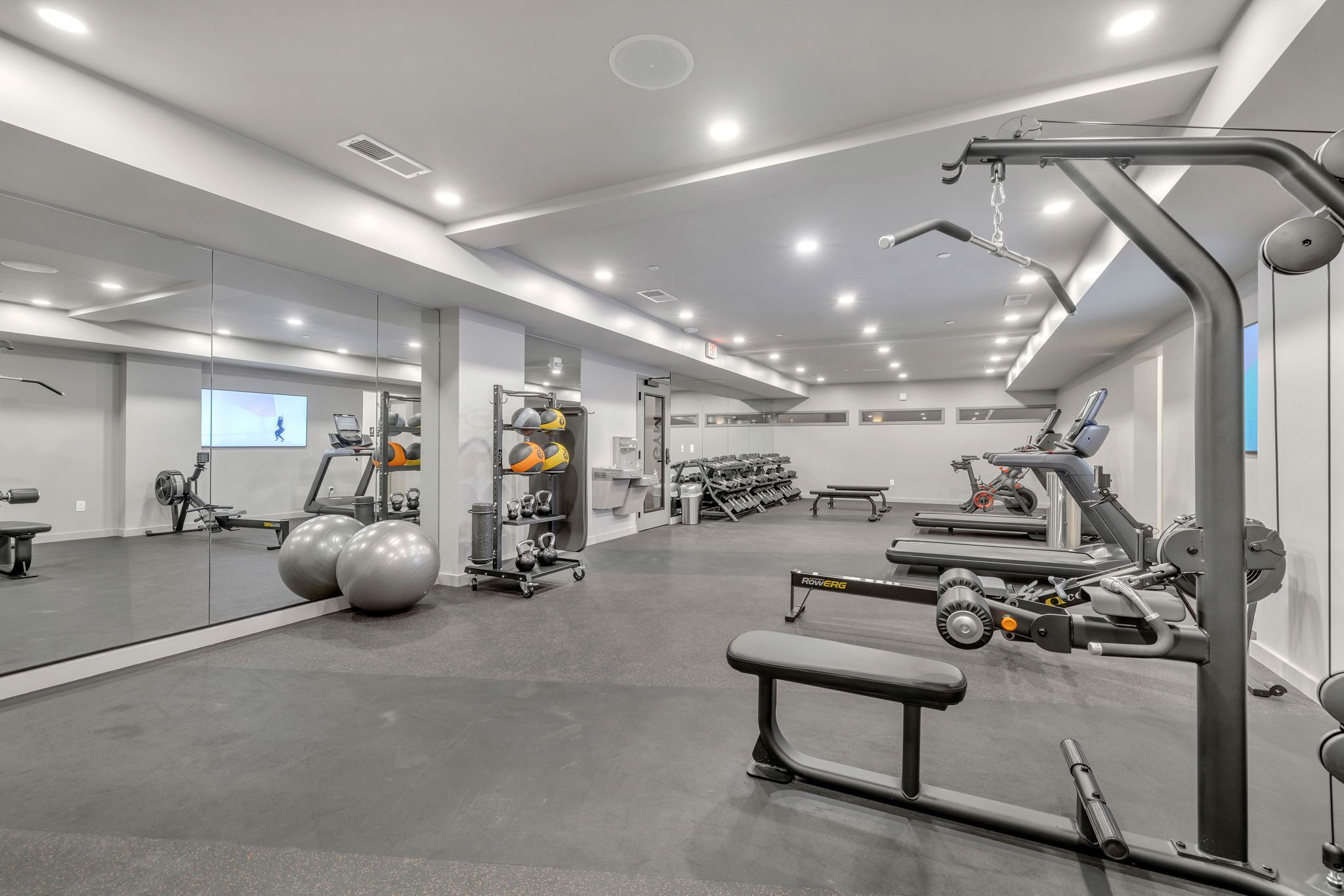 Une salle de sport moderne dotée de divers équipements d’exercice, d’un mur miroir et d’un aménagement propre et spacieux.