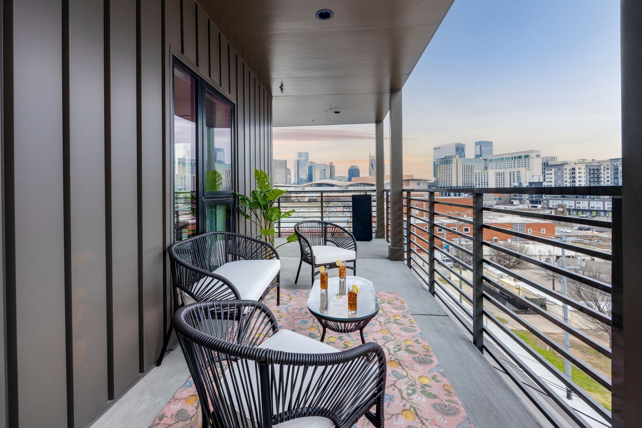 A balcony with wicker chairs, a small table, and a view of a cityscape.