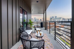 A balcony with wicker chairs, a small table, and a view of a cityscape.
