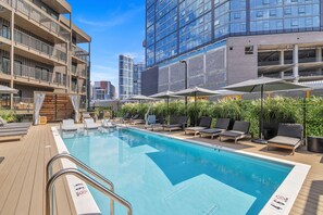 Una piscina en la azotea con sillones de descanso, una terraza de madera y vistas de edificios circundantes.