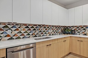 Een moderne keuken met witte kasten, een RVS vaatwasser en een betegelde spatwand met een geometrisch patroon.