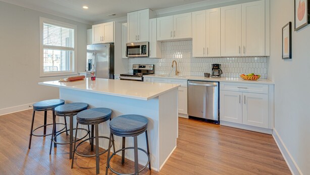 A modern kitchen with white cabinets, a central island with stools, stainless steel appliances, and a tiled backsplash. - Modern Melrose-sleeps 8- Mins to Downtown Broadway (Nashville)