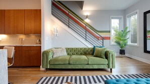 A modern living room with a green sofa, a striped rug, and a staircase with colorful railings. - Vivid Vocals - 4 Mins to Broadway - Rooftop Patio (Nashville)