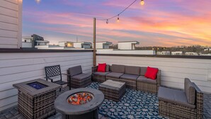 An outdoor patio with wicker furniture, a fire pit, and string lights against a sunset sky. - Nashville Nest - Rooftop Patio - Mins To Broadway (Nashville)