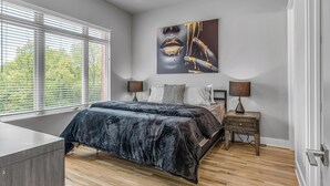 A modern bedroom with a large bed, a bedside table with a lamp, and a window with blinds. - Nashville Nest - Rooftop Patio - Mins To Broadway (Nashville)