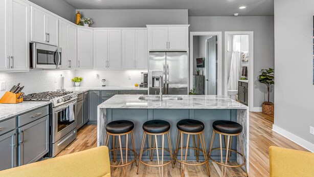 A modern kitchen with white cabinets, stainless steel appliances, a marble island with bar stools, and a wooden floor. - Nashville Nest - Rooftop Patio - Mins To Broadway (Nashville)