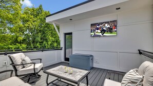 Una terraza con mobiliario exterior, un televisor en la pared y un enfriador azul grande.