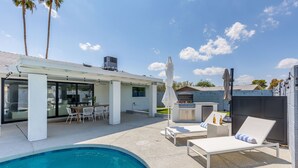 Un espace piscine extérieur moderne, doté d’un barbecue, de chaises longues et d’un patio couvert.