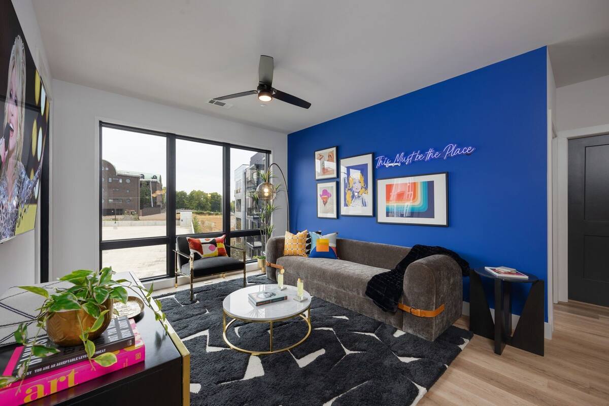 A modern living room with a blue accent wall, a large window, and a ceiling fan.