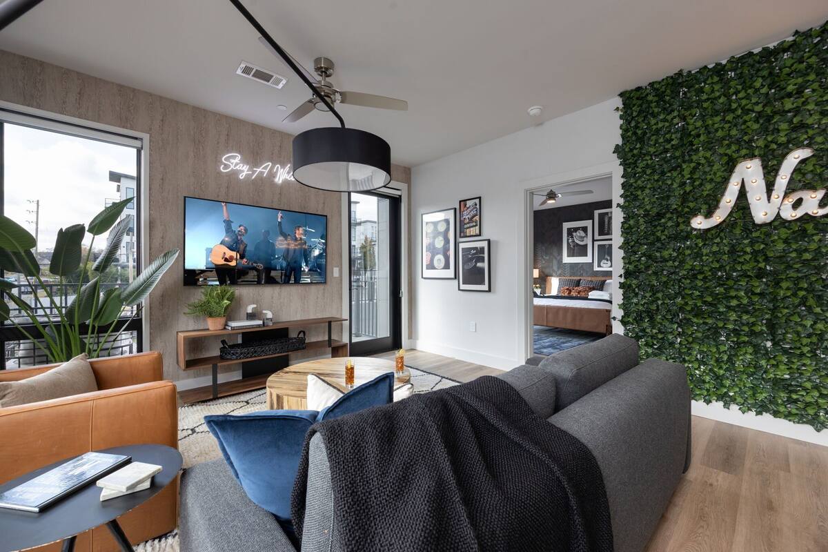 A modern living room with a flat-screen TV, a ceiling fan, and a green wall with a 'Na' sign.